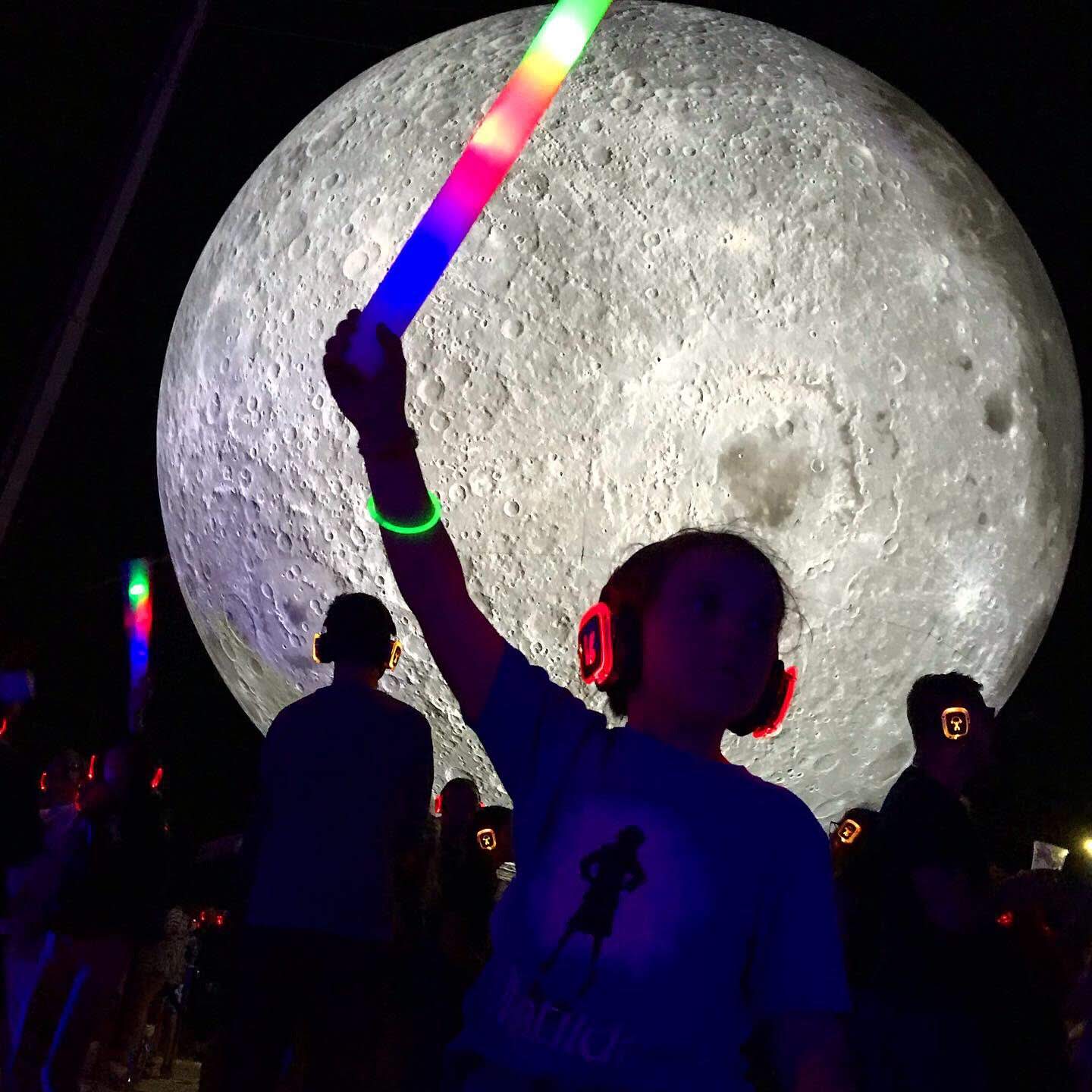 A boy waves a light wand in front of an illuminated moon