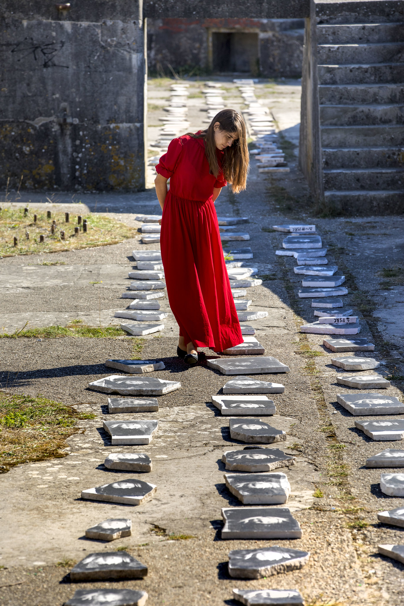 A woman wearng a bright red dress walks amongst stones