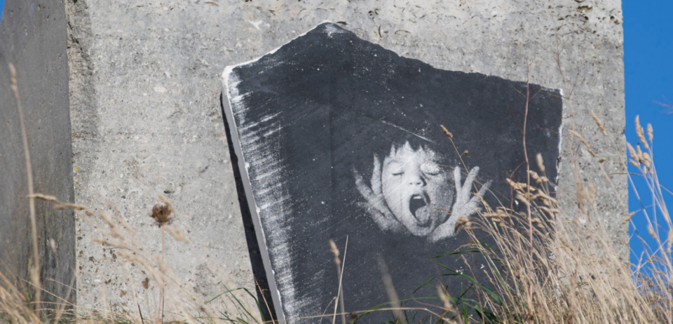 An image of a biys face screaming imprinted in black and white on the surface of a flat stone