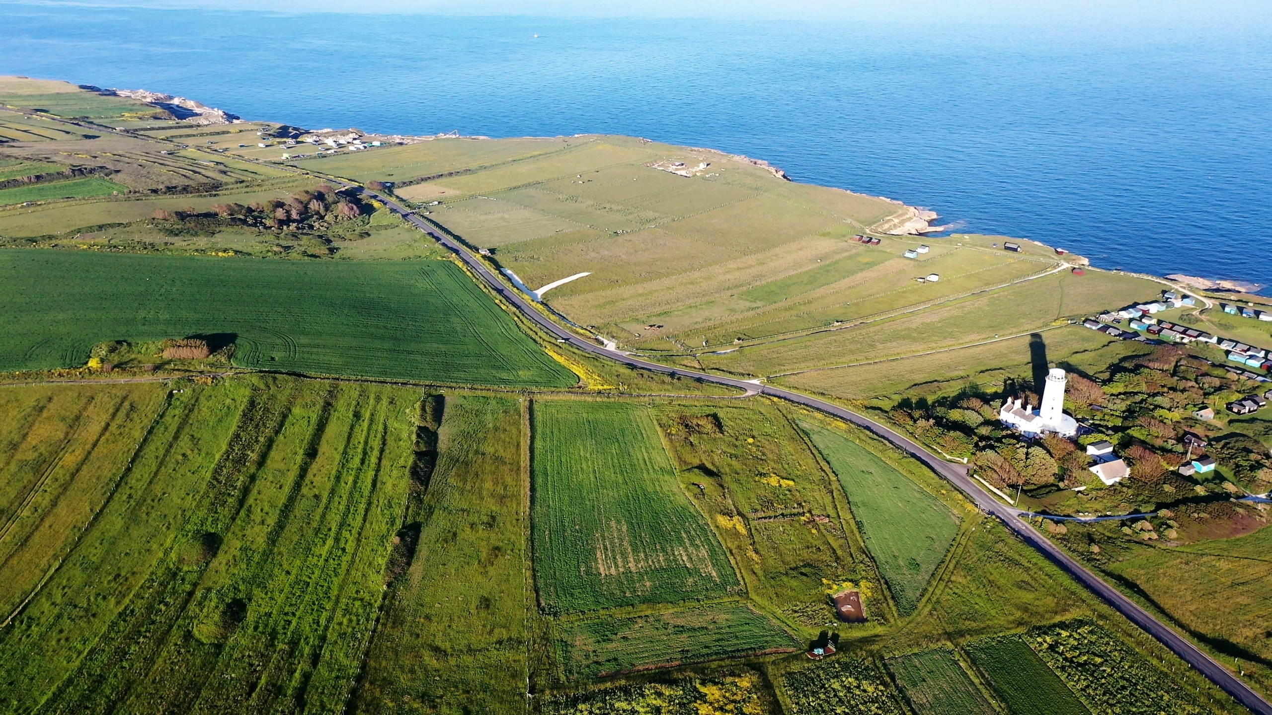 Birds eye view of a green landscape near the sea with a white lighthouse