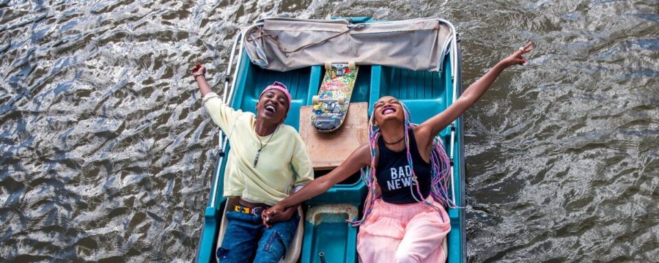 two women laughing looking up at the sky from a small blue boat on a lake
